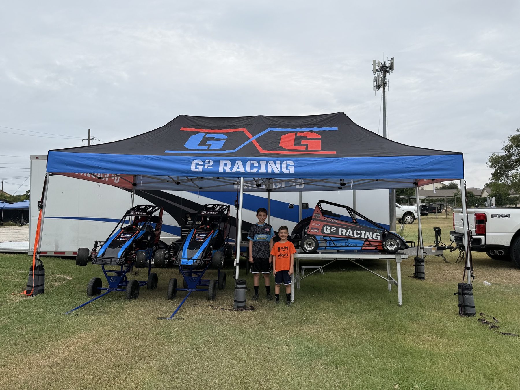 Connor and Ryan standing under the G² Racing canopy with cars and trailer