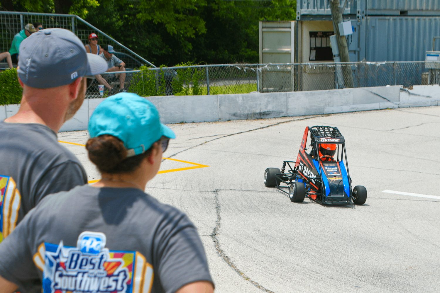 Two people watching a quarter midget from the fence line