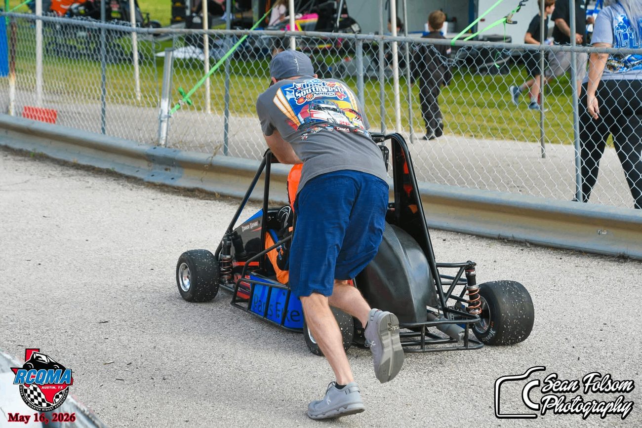 Sean Guthrie pushing a quarter midget away from the fence line